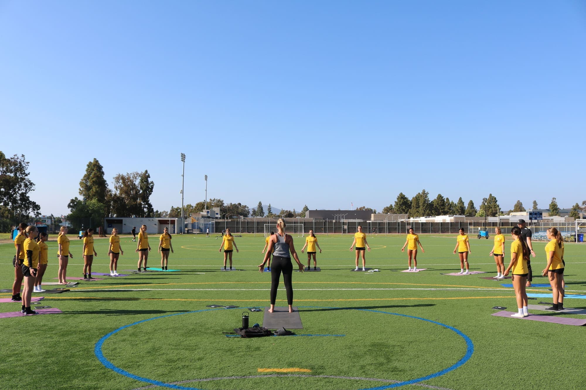 Allie Chapman leading athletes in a standing mindfulness session on a turf field