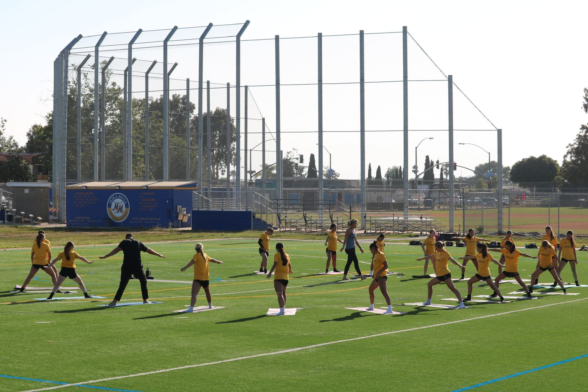 Athletes practicing Warrior II on a turf field during a Mind Body Athletes session