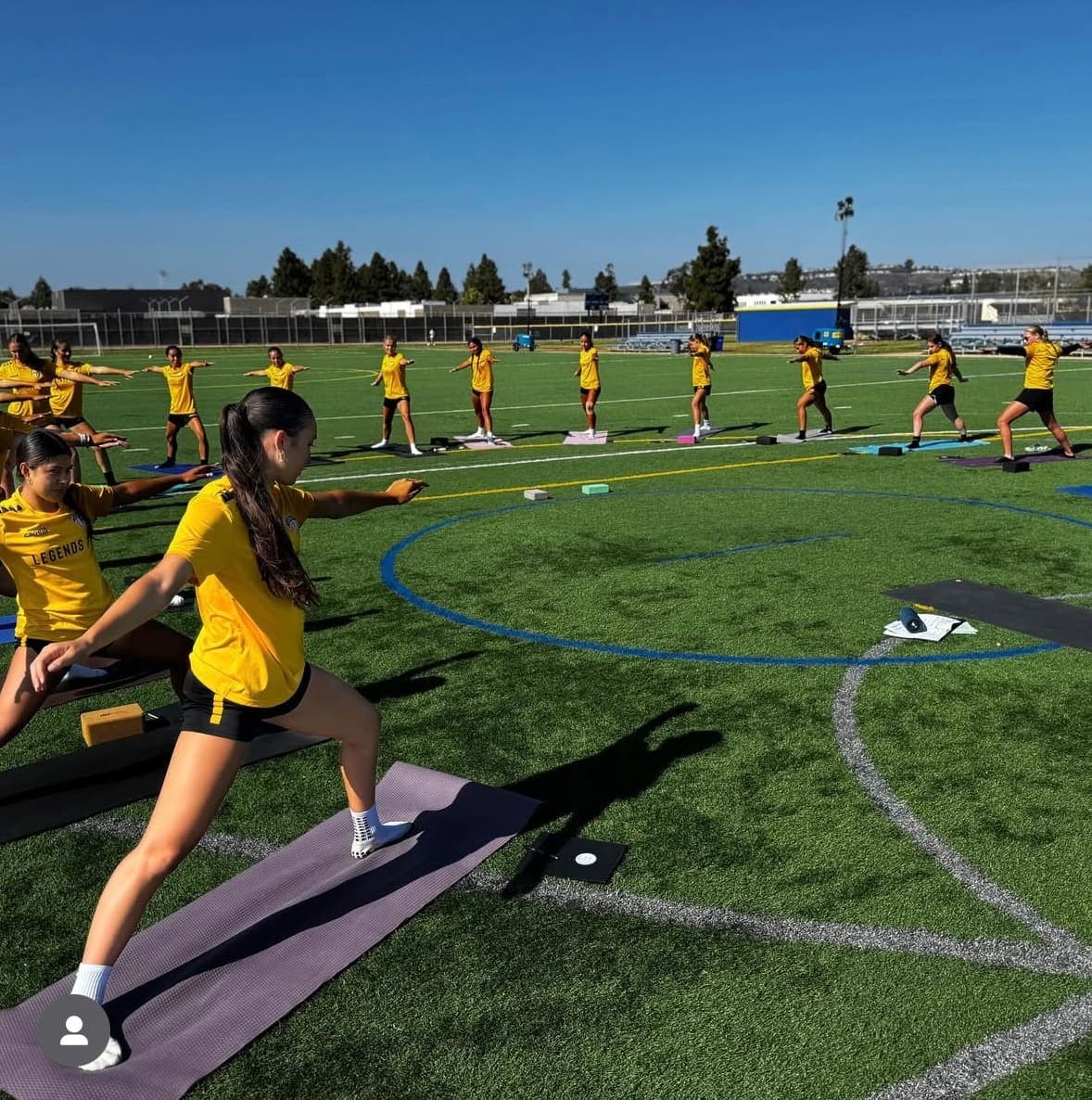 Athletes holding Warrior II on a turf field during a Mind Body Athletes session