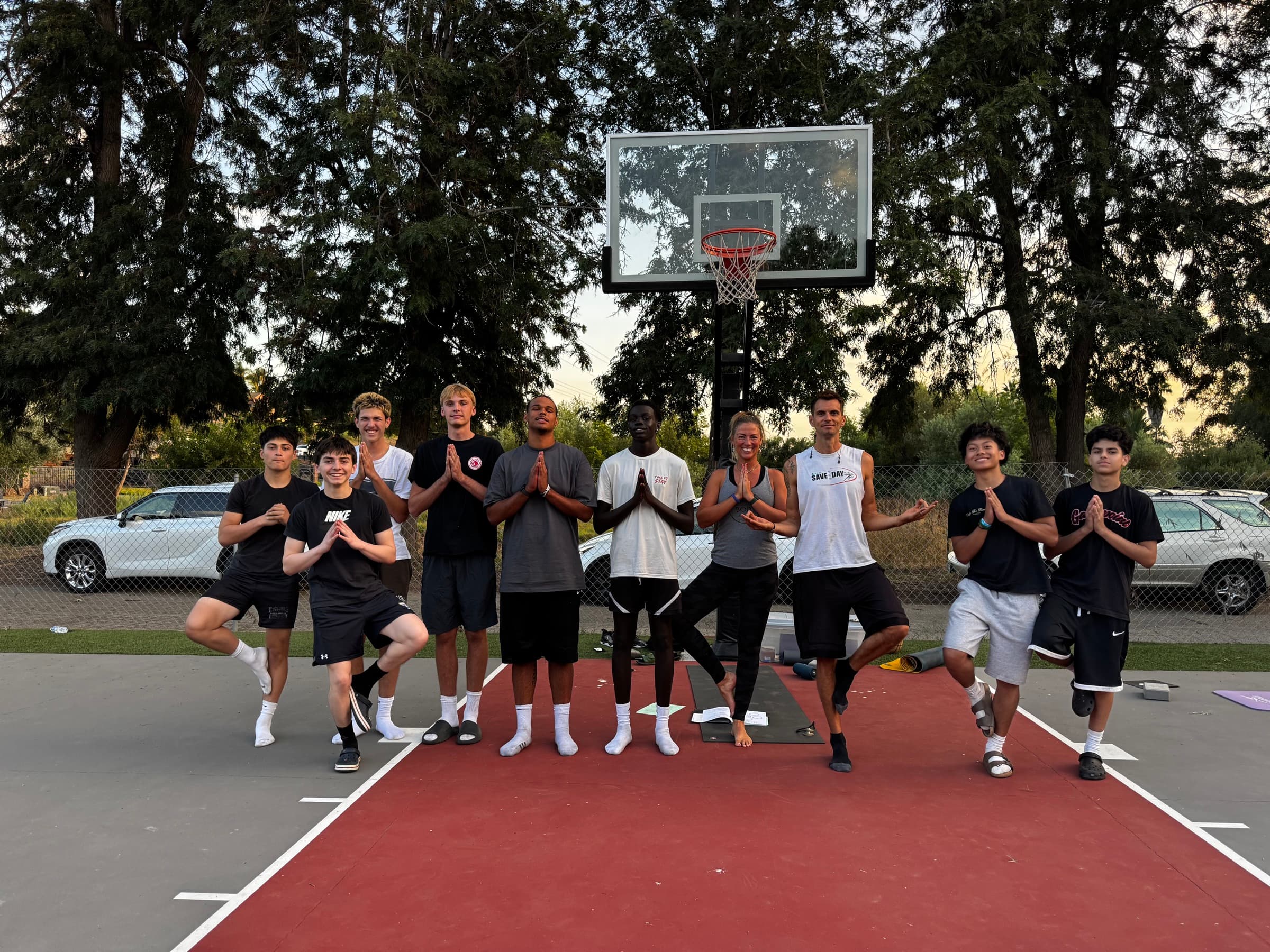 A boys basketball team holding tree pose with Allie Chapman on an outdoor court