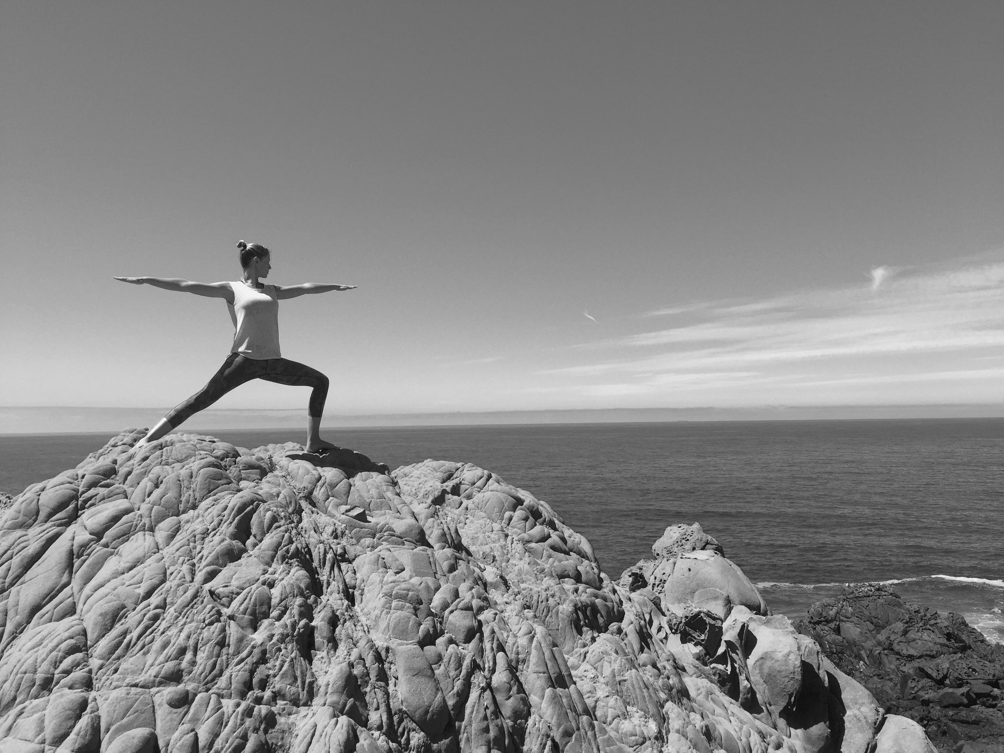 Person practicing yoga on rocky cliffs overlooking the ocean